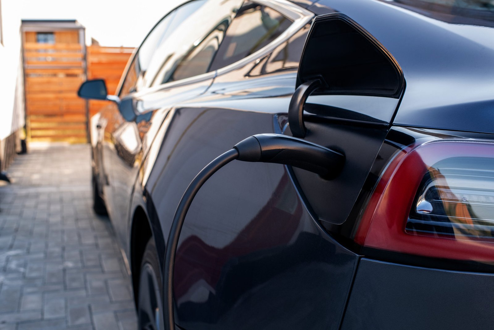 Close-up of a black electric vehicle plugged into a charger at a home charging station.