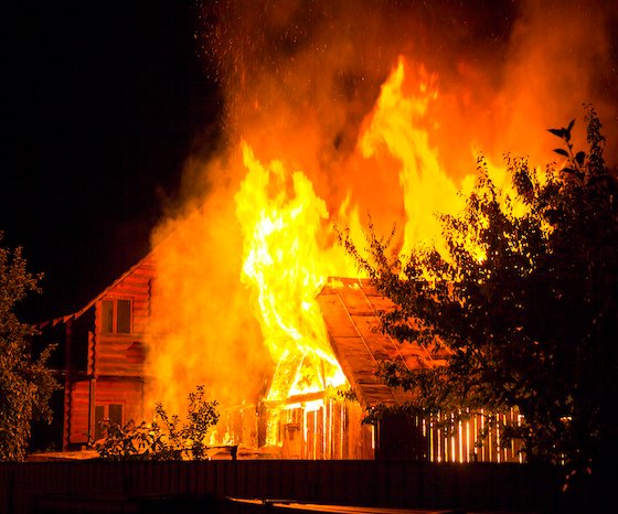A wooden house engulfed in flames at night, representing the severe fire risks caused by undiagnosed electrical faults or power tripping issues.
