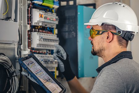 Licensed electrician in uniform servicing a residential switchboard, representing fault diagnosis and electrical repair services in Perth.