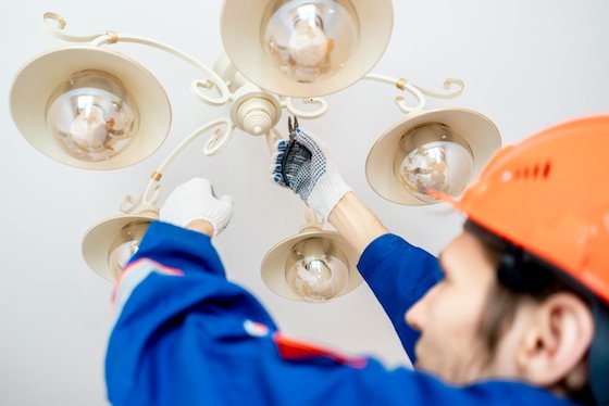Licensed electrician in Quinns Rocks standing on a ladder repairing a ceiling light fixture — STB Electrical Perth.